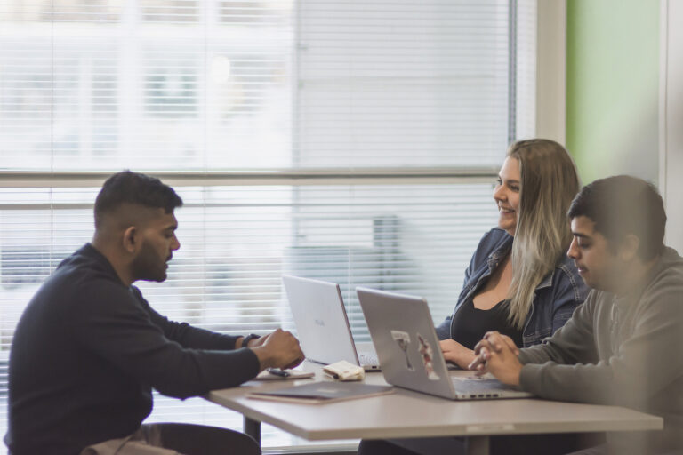 Kolme opiskelijaa istuu pöydän ääressä.