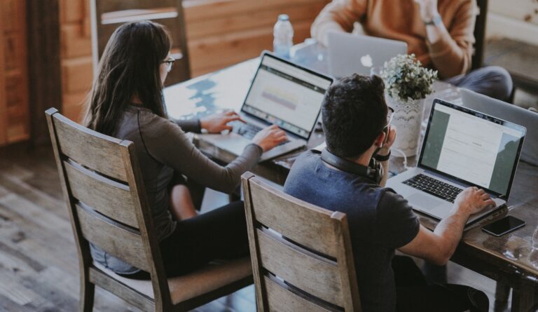 Kaksi henkilöä istuu vierekkäin pöydän ääressä ja työskentelee läppäreillä.